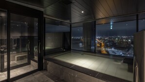 A modern bathroom with a glass-enclosed shower, a bathtub, and a view of a cityscape at night. - Tokyu Stay Hakodate Asaichi Akarinoyu (Hakodate)
