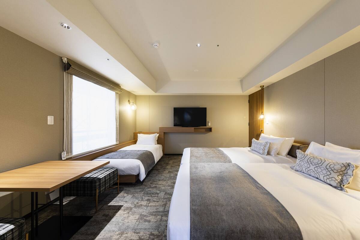 Una habitación de hotel con dos camas, televisión, escritorio y ventana.