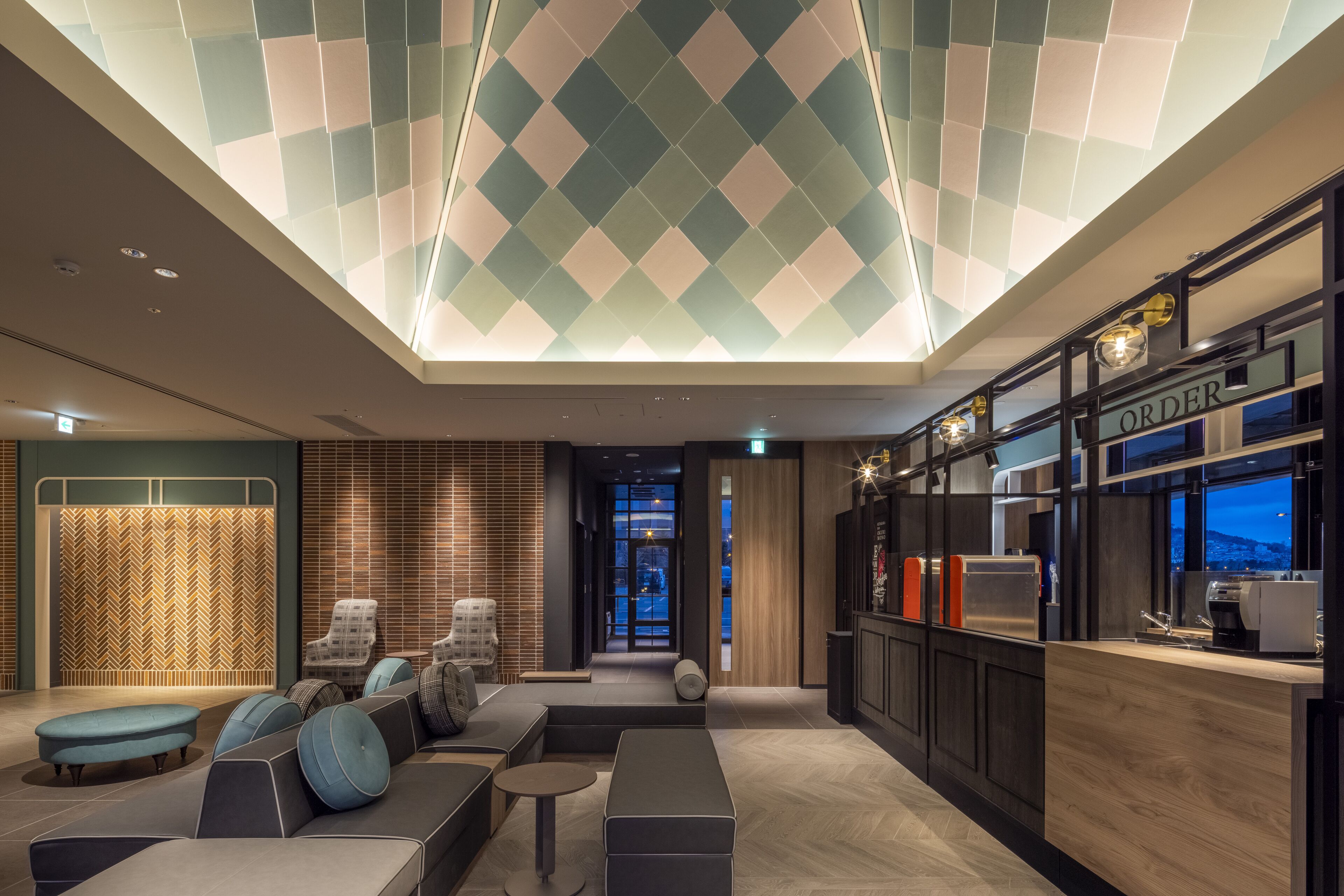 A modern hotel lobby with a seating area, a reception desk, and a view of the outside.