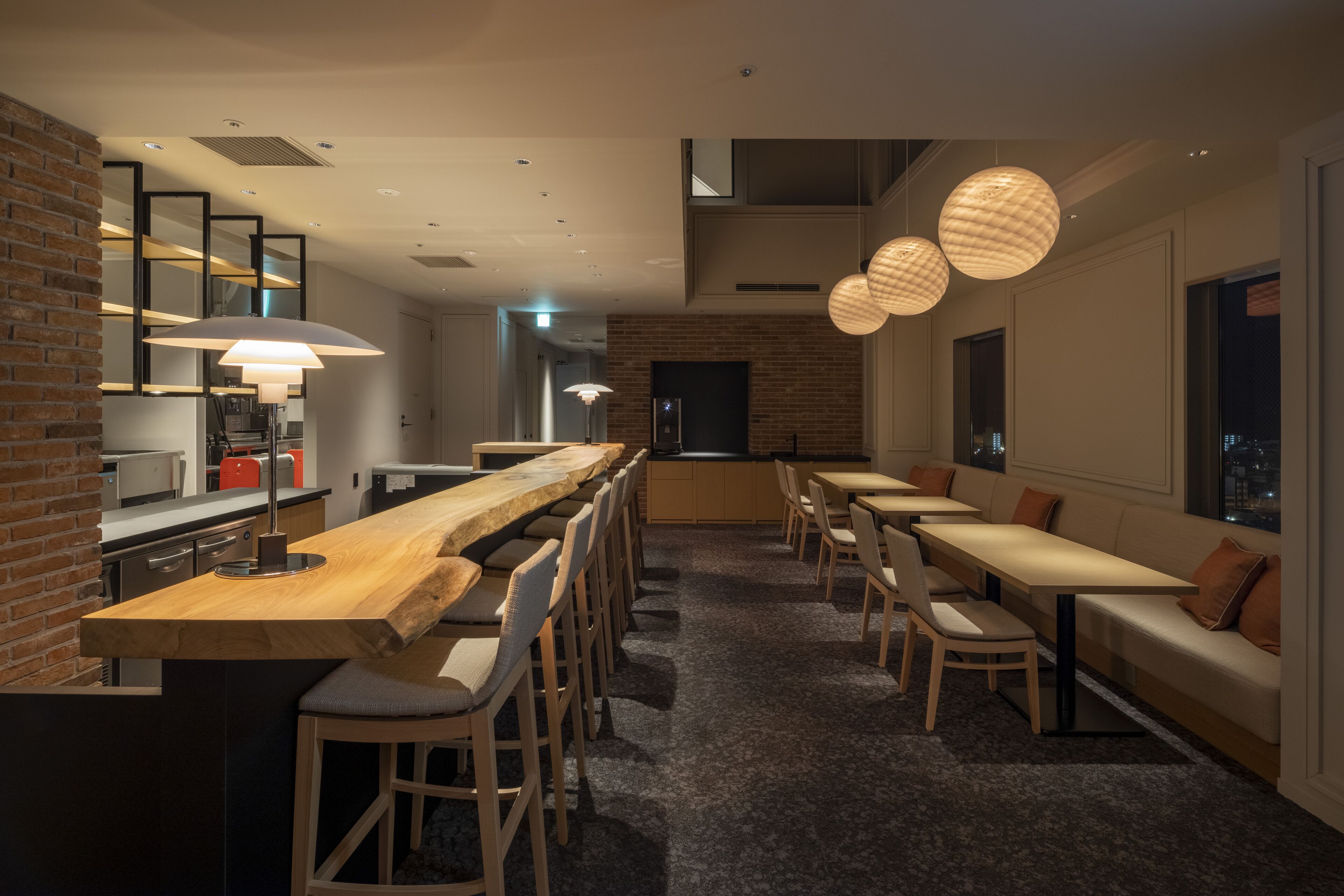 A modern restaurant with a long wooden counter, multiple seating areas, and pendant lighting.