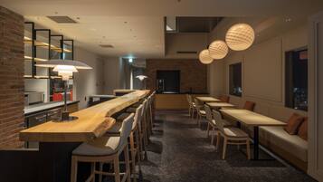 A modern restaurant with a long wooden counter, multiple seating areas, and pendant lighting.