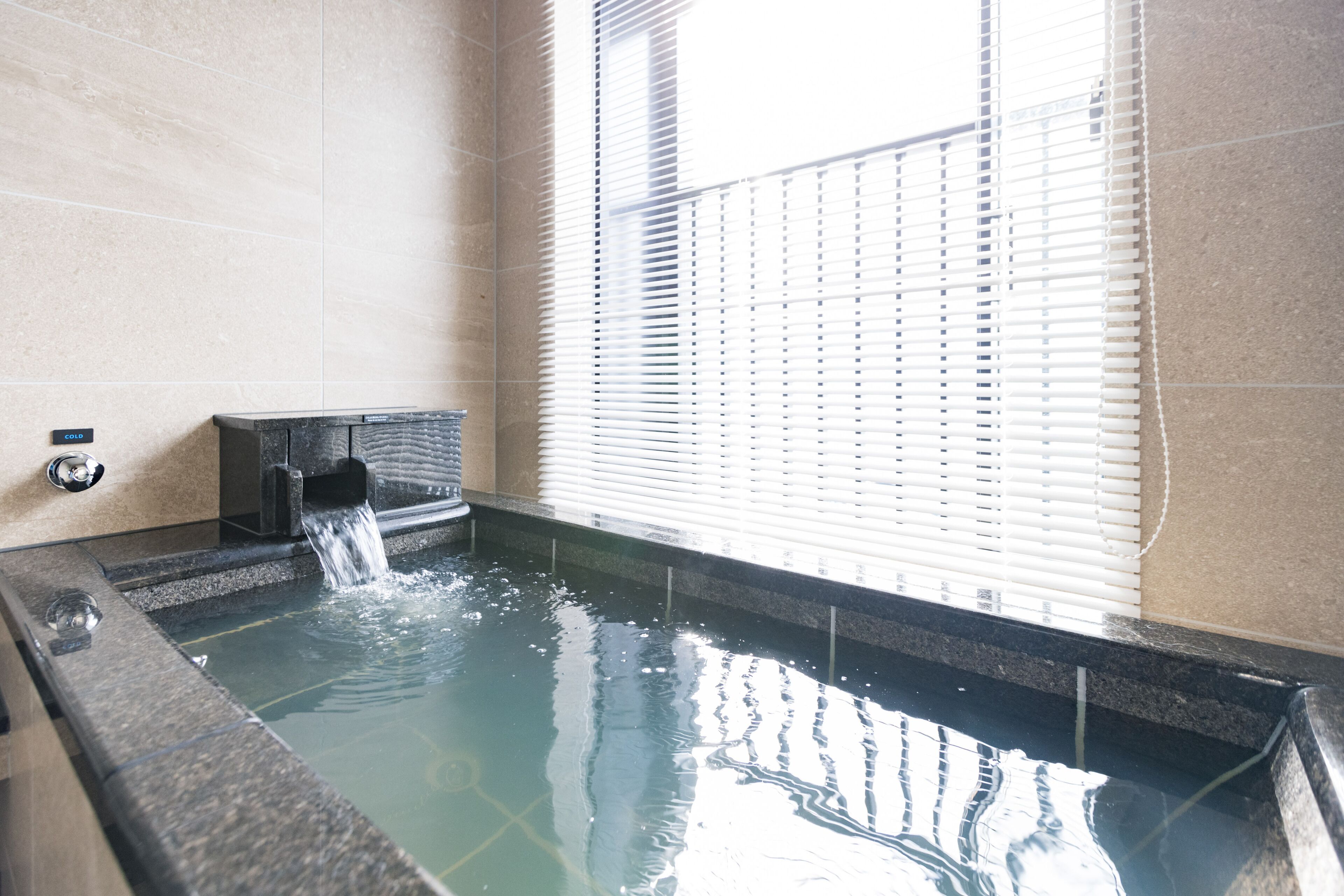A spa area with a hot tub, a water feature, and a window with blinds.
