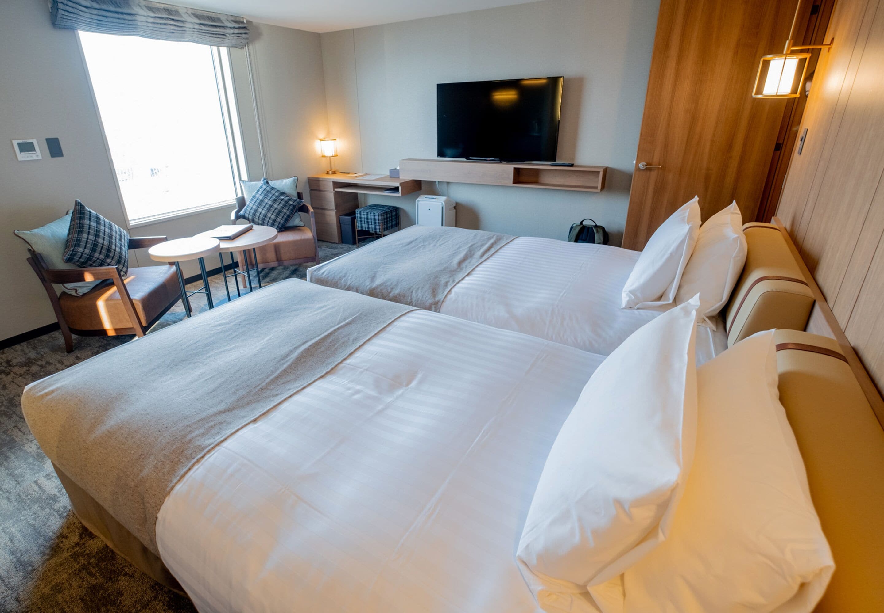 A hotel room with two beds, a TV, a desk, and a chair.