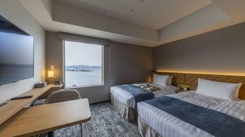 Habitación de hotel con dos camas, un escritorio, un televisor y una ventana con vistas al agua.