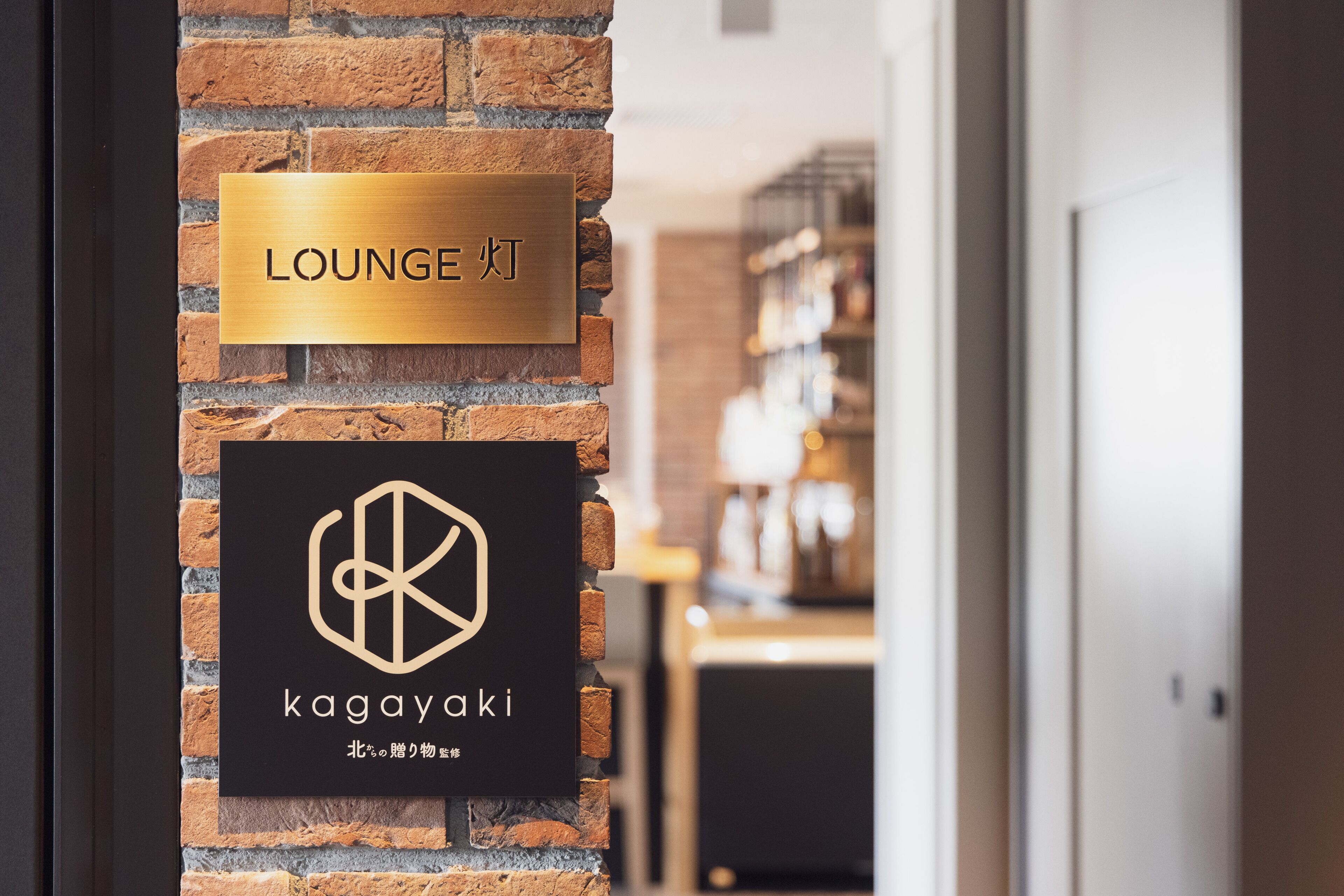 A brick wall with a sign indicating a lounge area and a logo for 'kagayaki'.