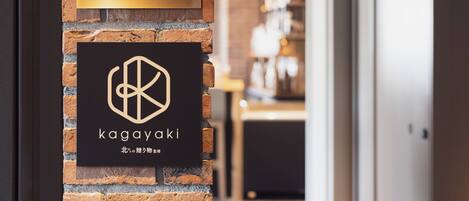 A brick wall with a sign indicating a lounge area and a logo for 'kagayaki'.
