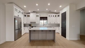 Eine moderne Küche mit weißen Schränken, einer zentralen Kochinsel und einem Edelstahl-Kühlschrank.