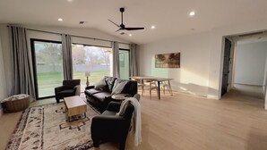 Ein großzügiges Wohnzimmer mit Sofa, Sessel und Couchtisch, großen Schiebeglasüren zum Garten und einem Deckenventilator.