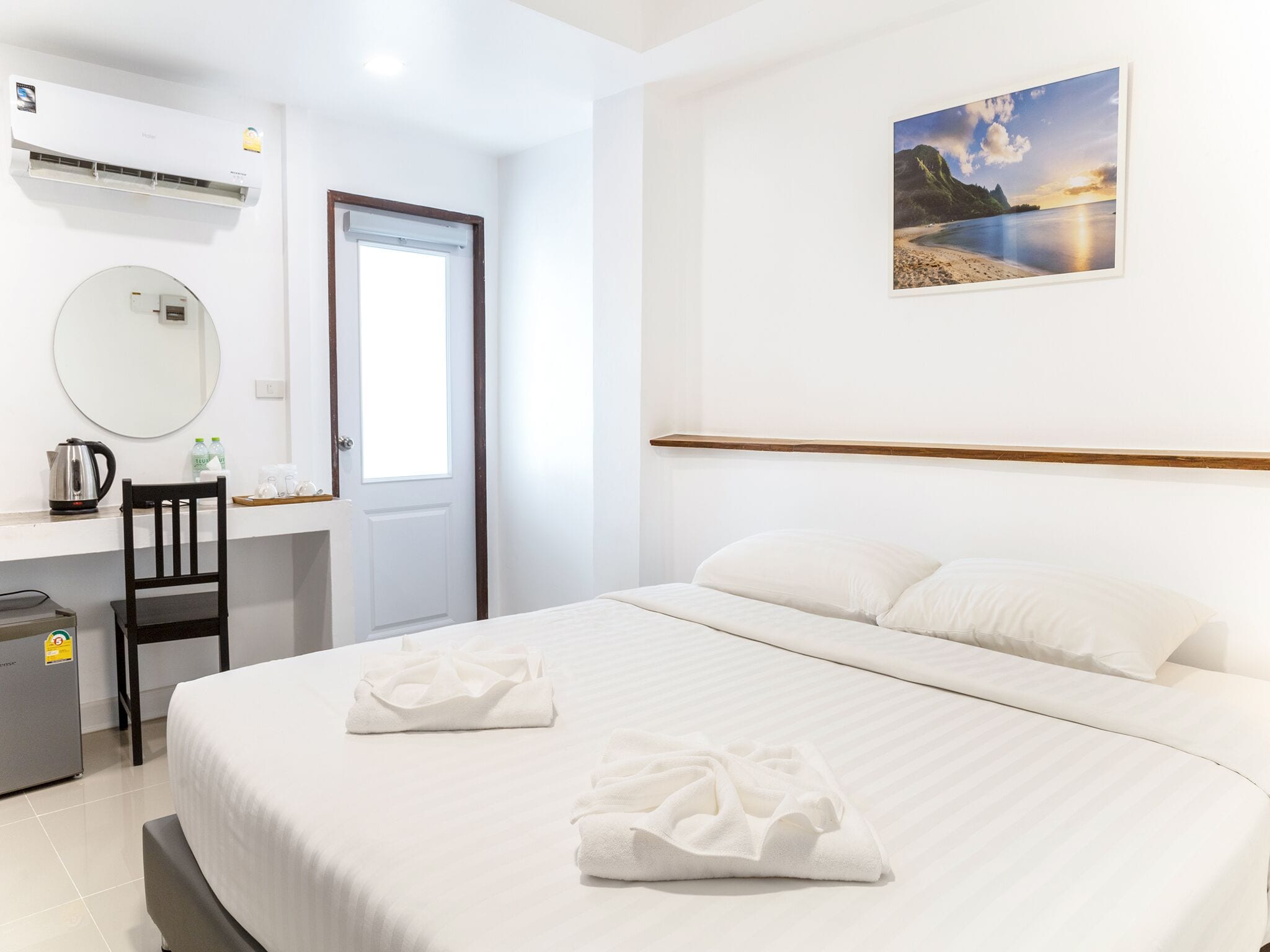 Una camera d'albergo con un letto, una scrivania, una sedia, uno specchio, un quadro appeso al muro e un condizionatore d'aria.