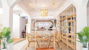 A cafe with wicker furniture, a hanging light fixture, and a sign reading "Grand Cafe".