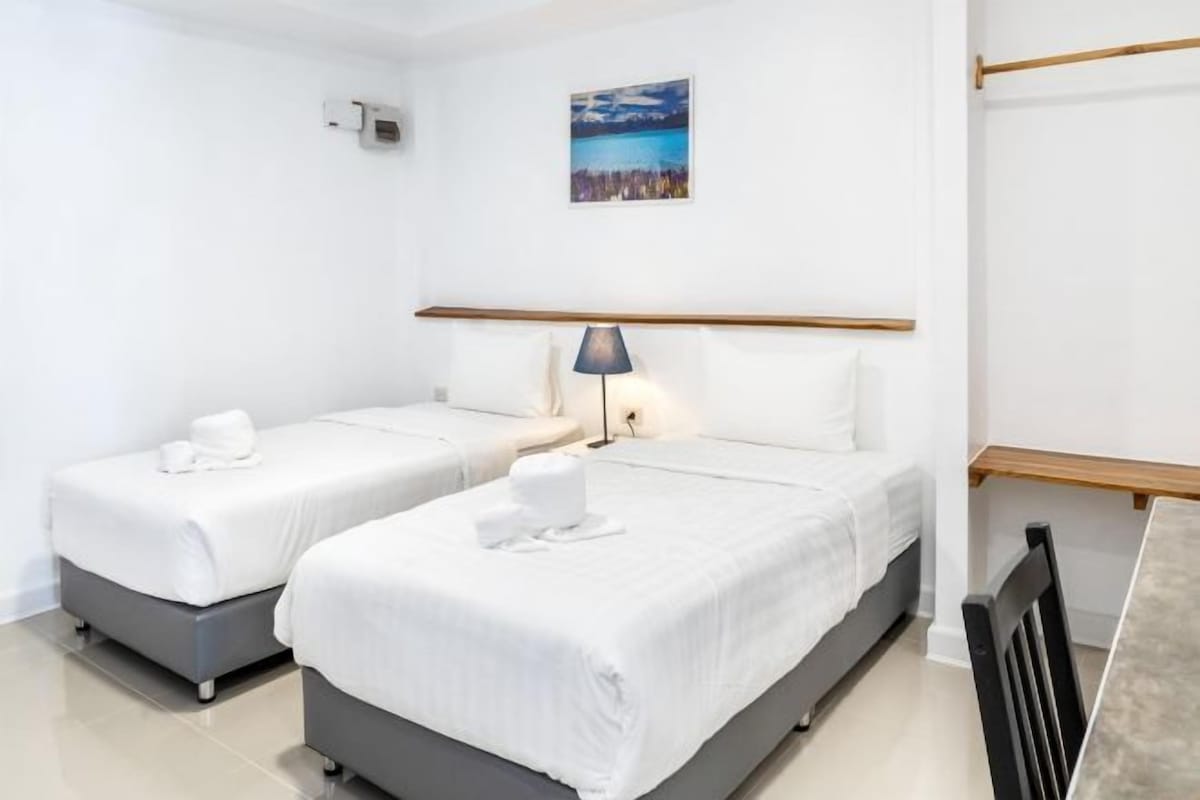 A hotel room with two beds, a nightstand, a lamp, and a picture on the wall.