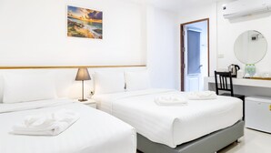 A hotel room with two beds, a desk, a chair, a small refrigerator, a lamp, and a painting on the wall.