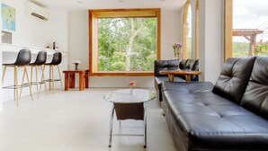 A modern living room with a black leather sofa, a round glass coffee table, and a dining area with a wooden table and chairs.