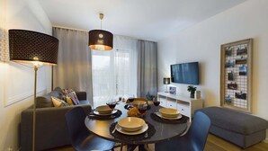 A modern living room with a dining area, featuring a round table with chairs, a sofa, a TV, and a decorative wall piece. - Modern apartment in Krakow | Parking | Close to the train station (Kraków)