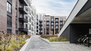 A modern urban courtyard with a paved walkway, surrounded by multi-story residential buildings with balconies and a bike rack. - Modern apartment in Krakow | Parking | Close to the train station (Kraków)