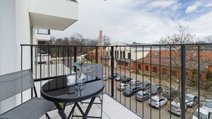 A balcony with a glass table and chairs, overlooking a parking area and buildings. - Modern apartment in Krakow | Parking | Close to the train station (Kraków)
