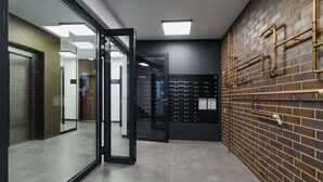 A modern hallway with glass doors, a brick wall with metal pipes, and a control panel with numbered buttons. - Modern apartment in Krakow | Parking | Close to the train station (Kraków)