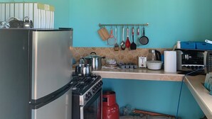Uma cozinha com frigorífico, fogão e micro-ondas em aço inoxidável. Há um relógio na parede e diversos utensílios de cozinha pendurados acima da bancada.