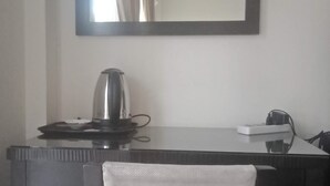 Habitación de hotel con escritorio, tetera, silla y un espejo grande en la pared.