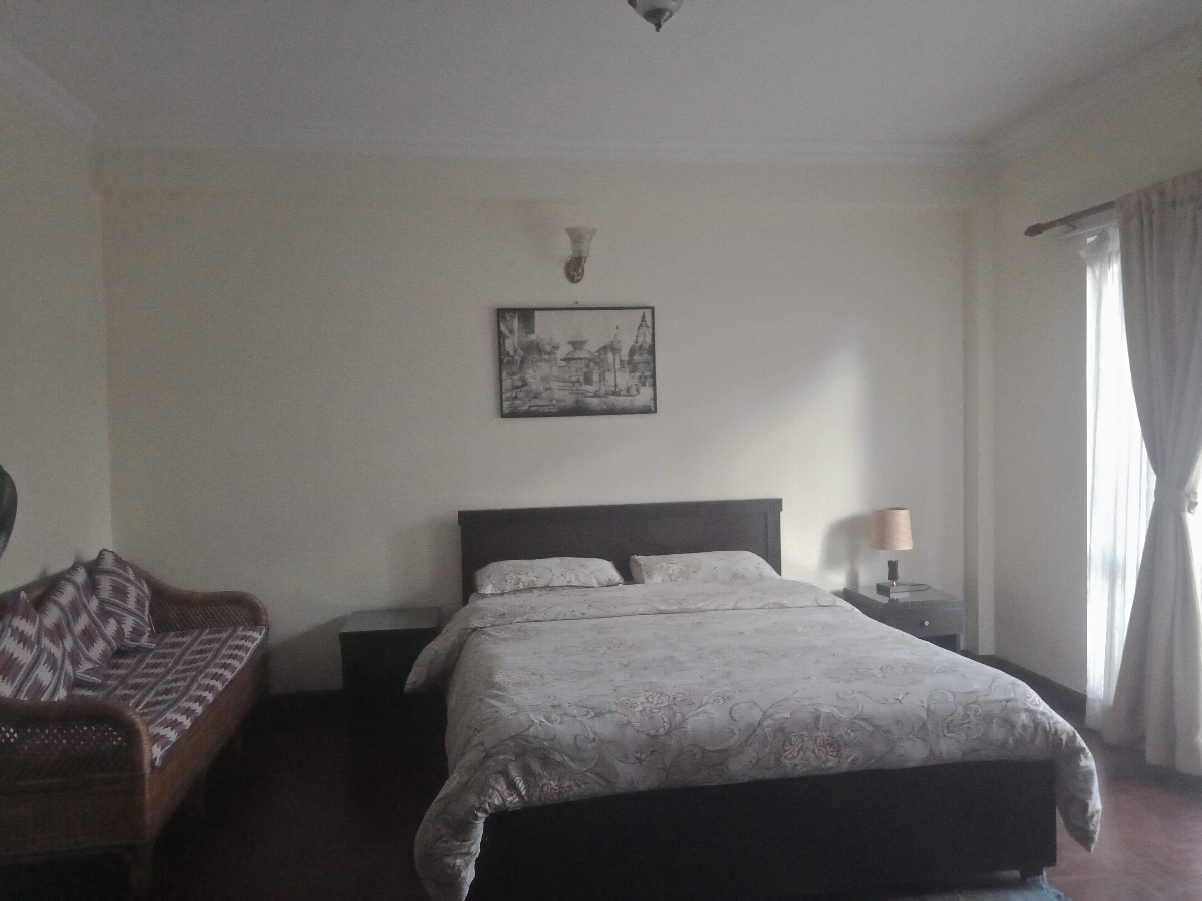 Un dormitorio con cama, mesita de noche, lámpara, sofá y un cuadro colgado en la pared.