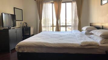 Una habitación de hotel con una cama, televisión, escritorio y ventana con cortinas.