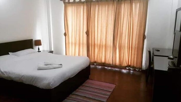 Una habitación de hotel con cama, escritorio, silla, televisión y ventana con cortinas.