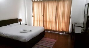 Una habitación de hotel con cama, escritorio, silla, televisión y ventana con cortinas.