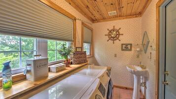 A laundry area with a washing machine, a sink, and a window with blinds.