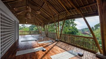 Une vaste terrasse en bois, dotée de tapis de sol pour faire de l’exercice, d’un plafond en bambou et offrant une vue sur une végétation luxuriante.