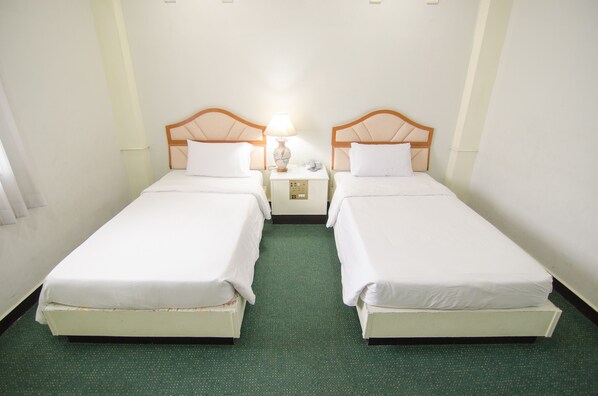 Habitación doble con dos camas individuales, una mesita de noche con lámpara y alfombra verde.