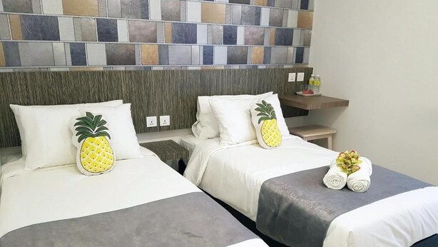Ein Hotelzimmer mit zwei Betten, jedes mit einem Kissen mit Ananas-Motiv und einem ordentlich gefalteten Handtuch.