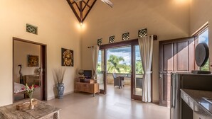 A spacious room with a wooden coffee table, a TV, and a view of the outdoors through a glass door. - Villa Kubu Agung (Ubud)