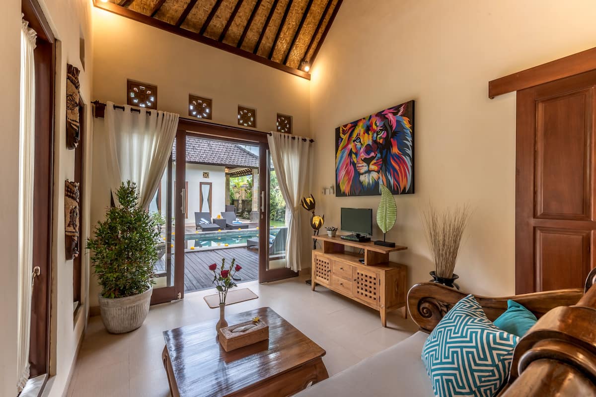 Amplia sala de estar con una mesa de centro de madera, un sofá con cojines estampados, un televisor sobre un mueble de madera y un cuadro grande en la pared.