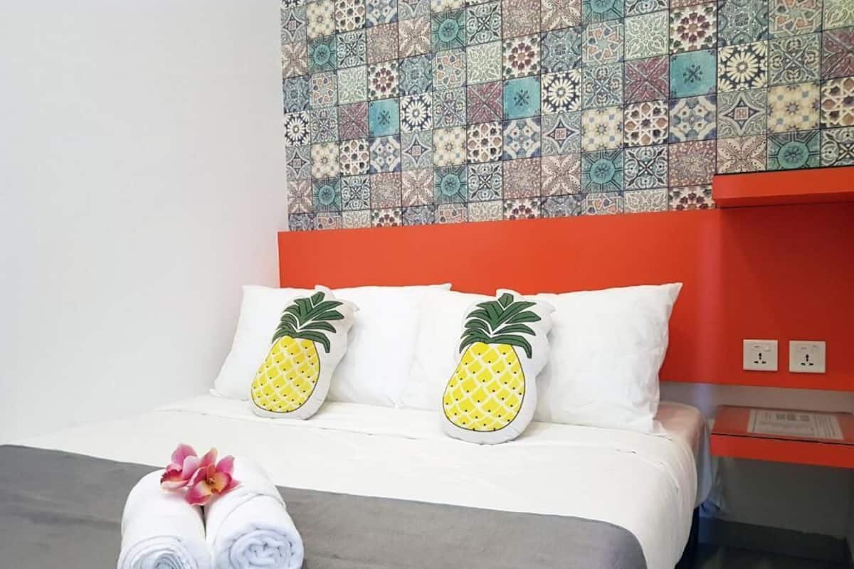 Ett hotellrum med en säng, två kuddar formade som ananas, en prydligt vikt handduk och en vägg täckt av mönstrade kakelplattor.