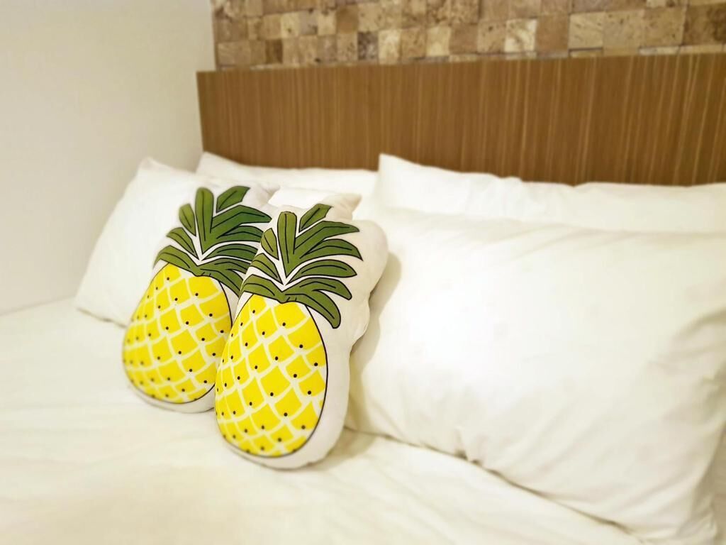 A bed with white bedding and two decorative pillows featuring a pineapple design.