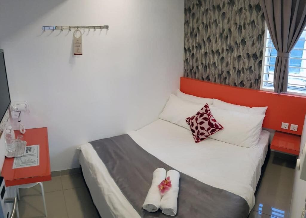 Een hotelkamer met een bed, een bureau met telefoon, een kapstok aan de muur en een raam met gordijnen.