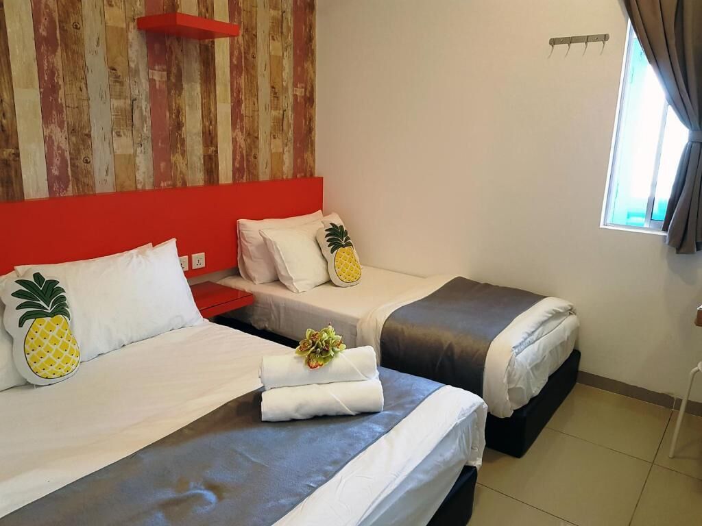 A hotel room with two beds, each with a pineapple pillow, a red headboard, and a window with curtains.