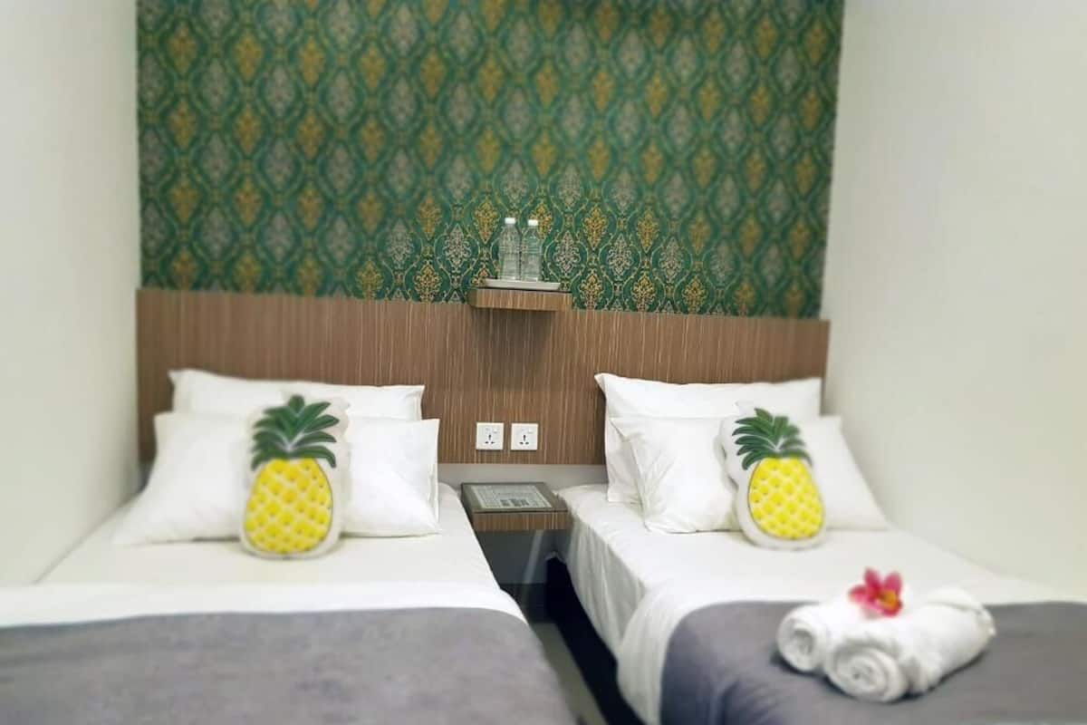 Ett hotellrum med två sängar, var och en med en ananaskudde, en vattenflaska på ett nattduksbord och en handduk med ett blommönster på en av sängarna.
