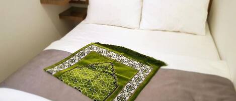 A neatly made bed with a patterned throw pillow and a bedside table with a lamp.