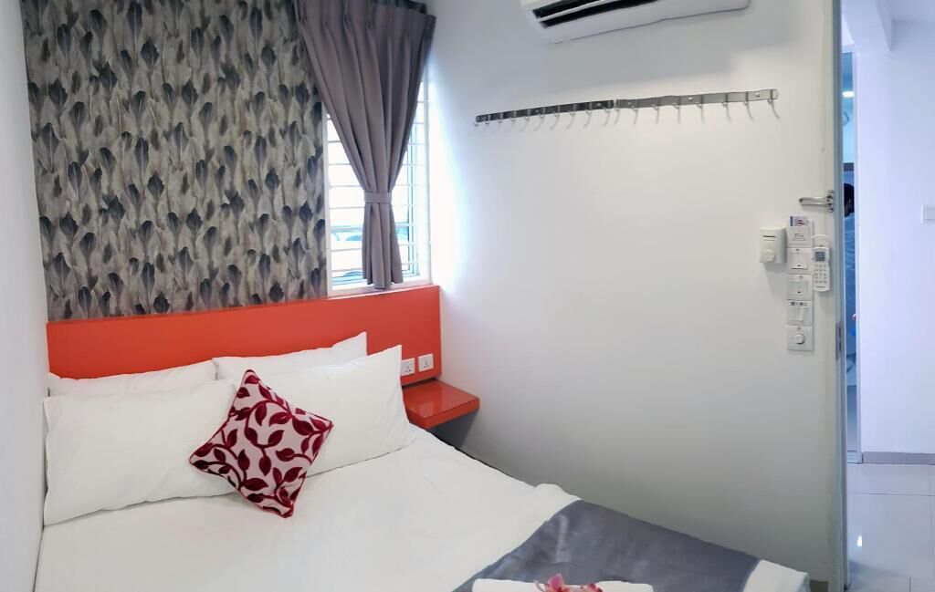 A hotel room with a bed, a red headboard, a window with curtains, and a wall-mounted air conditioning unit.