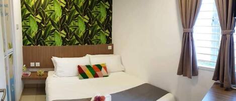 A hotel room with a bed, a nightstand, a wall with a leafy pattern, and a window with curtains.