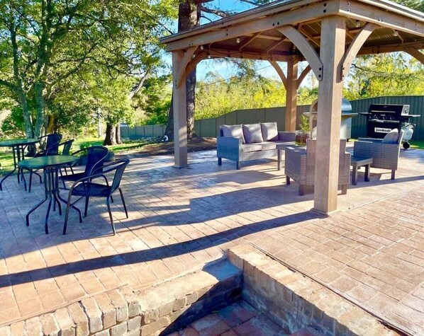 An outdoor patio with a pergola, outdoor furniture, and a grill area.