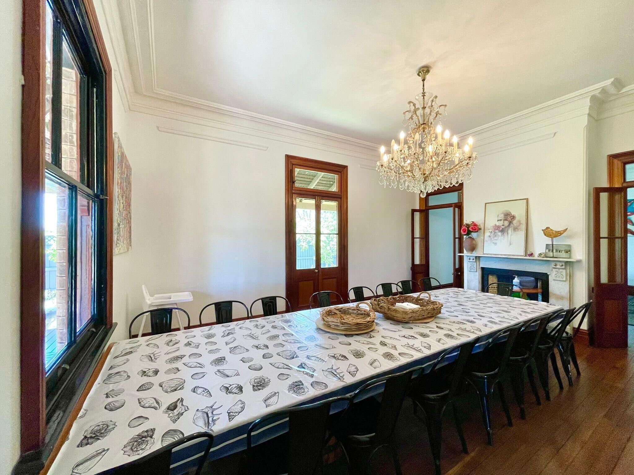 A dining room with a long table, chairs, a chandelier, and a fireplace.