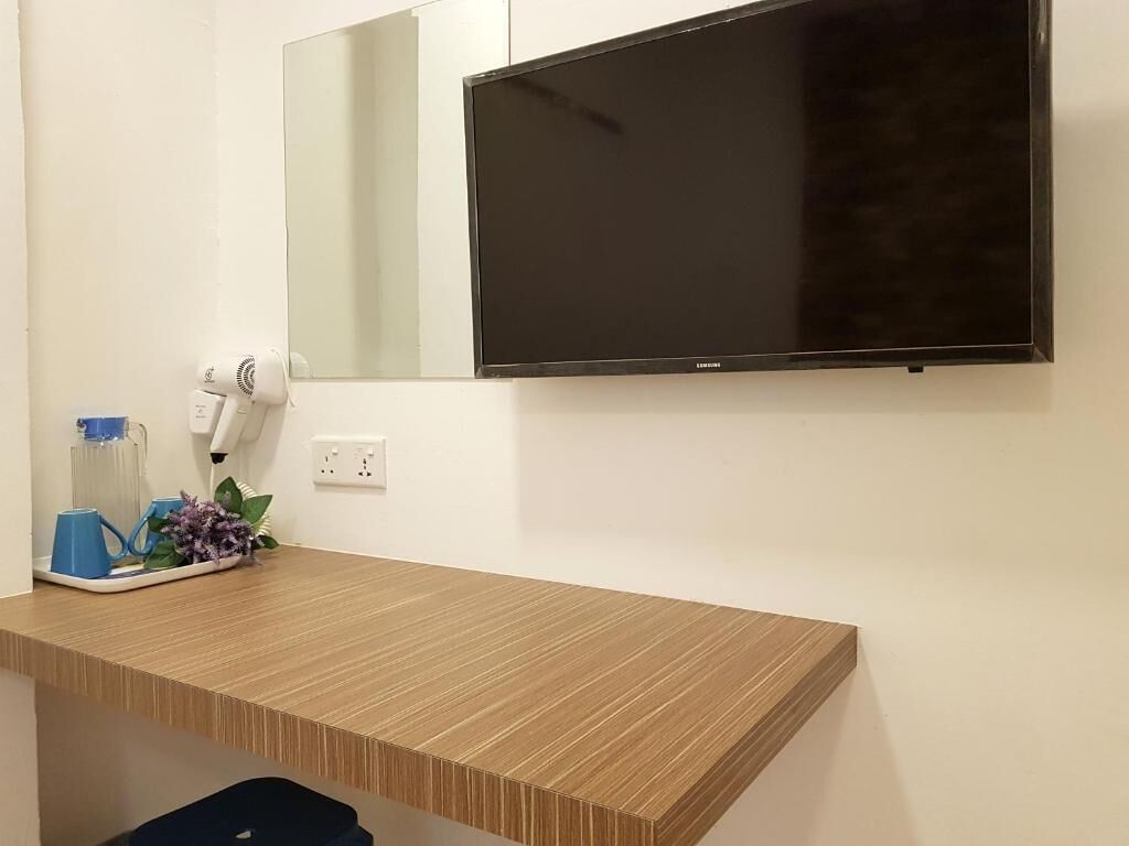 Un baño moderno con un mueble de tocador de madera, un televisor de pantalla plana montado en la pared y un secador de pelo sobre la encimera.
