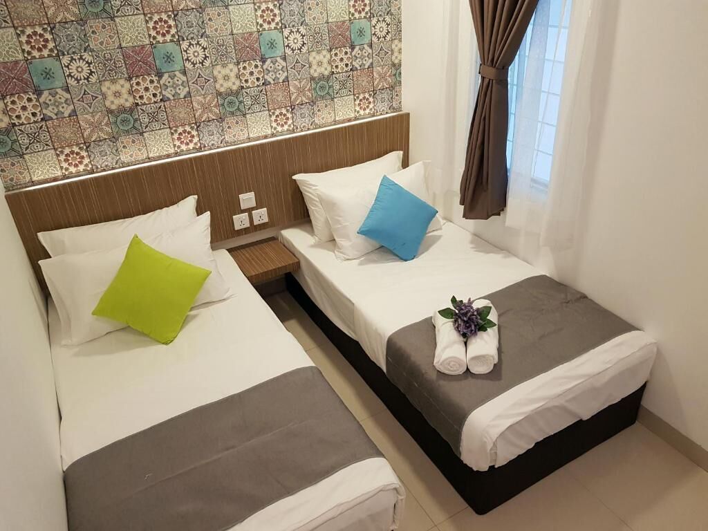 A hotel room with two beds, each with white linens and pillows, a small table, and a decorative tile wall.