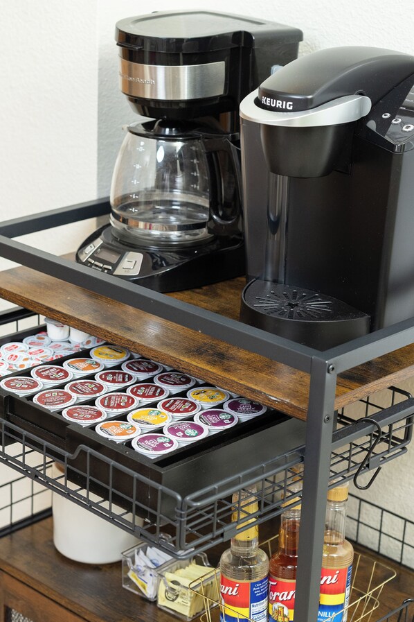 A coffee machine, a coffee maker, and a tray of coffee pods on a metal cart.