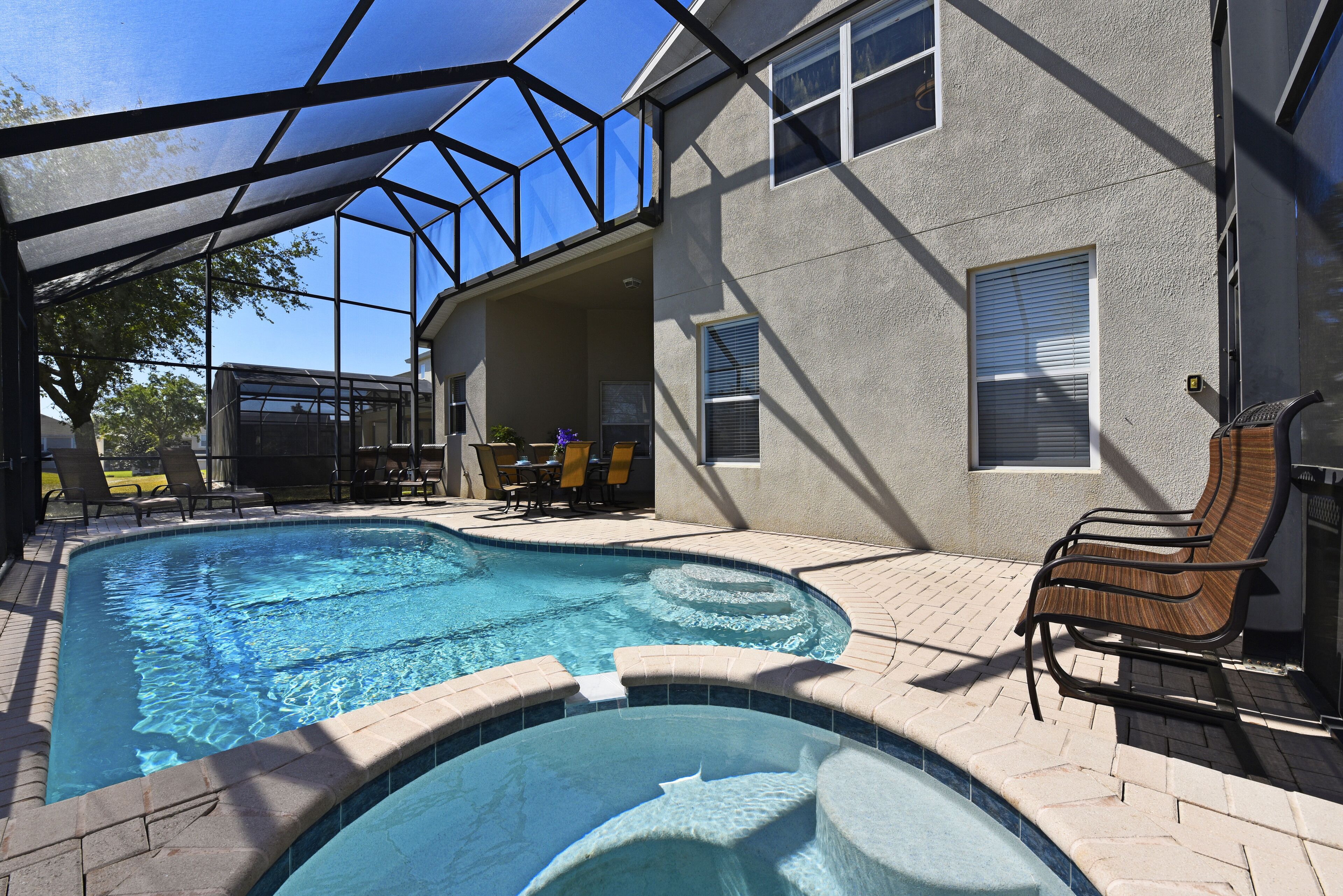 A swimming pool with a sunshade structure, a covered patio area, and a brick pathway.
