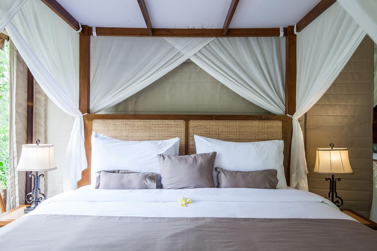 Un lit à baldaquin, deux lampes de chevet et une fleur sur le lit.