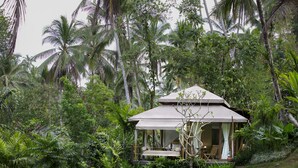 A secluded bungalow surrounded by dense tropical vegetation, featuring a covered porch with seating and a small table. - Galalima Glamping (Selemadeg)