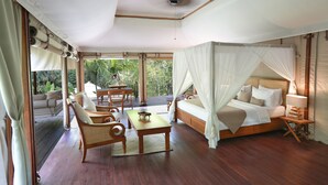 A spacious room with a large bed, a sitting area with chairs, a small table, and a view of greenery outside. - Galalima Glamping (Selemadeg)